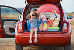 Das Bild zeigt ein kleines Mädchen dass neben Urlaubskoffern im Kofferraums eines Autos sitzt