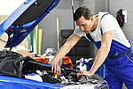 Das Bild zeigt einen KFZ Mechaniker vor der offenen Motorhaube eines Fahrzeugs