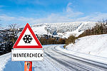 Das Bild zeigt eine Straße im Winter die mit Schnee bedeckt ist, davor steht ein Warnschild mit der Aufschrift Wintercheck.